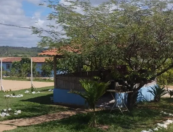 Quiosque de telhado colonial e cercado de bambu sob uma árvore grande, com uma mesa de metal ao lado